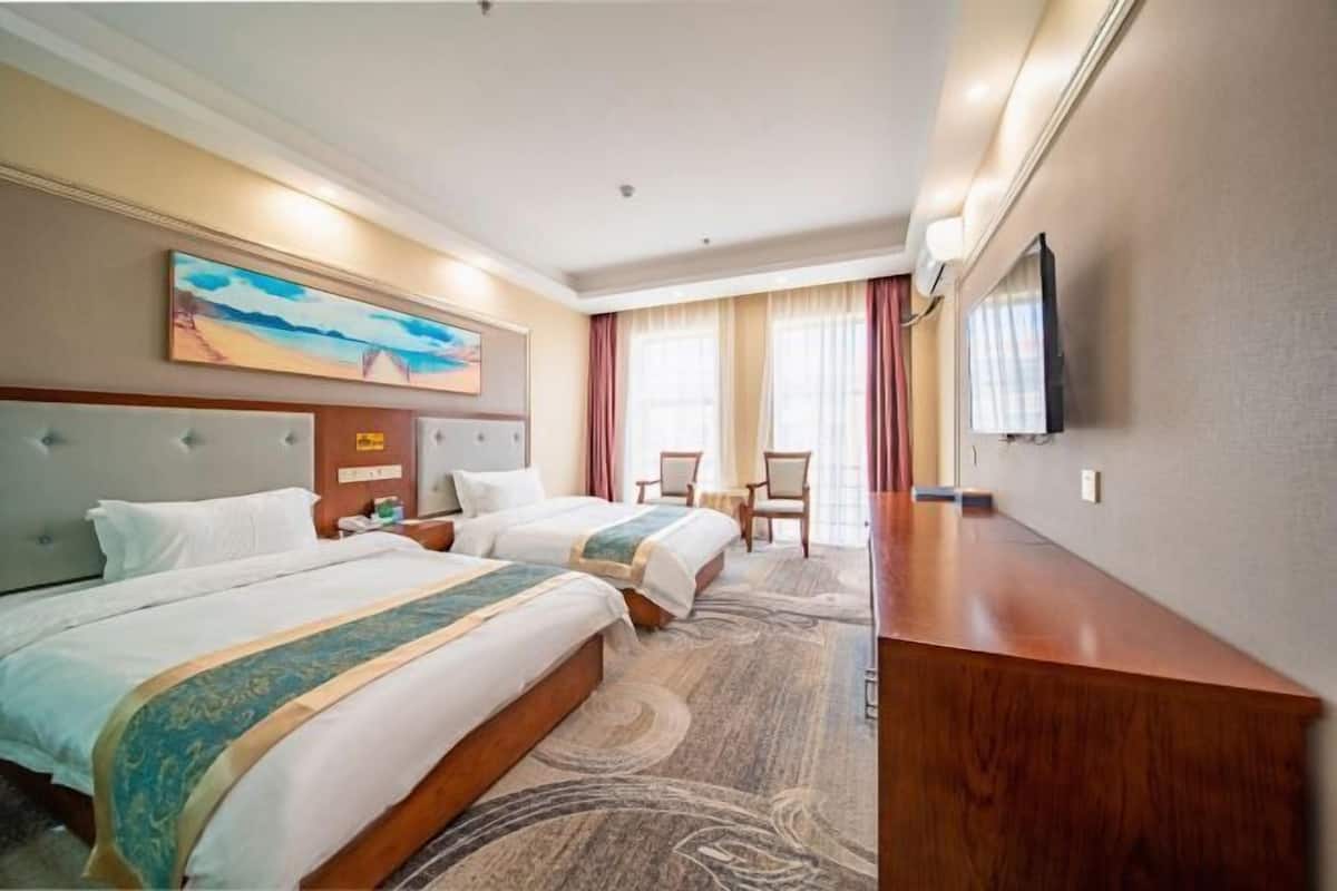 A hotel room with two beds, a TV, a desk, and a painting on the wall.