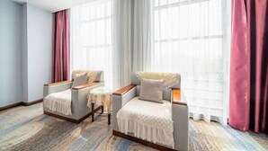 Habitación de hotel con dos sillones, una mesita redonda y un gran ventanal con cortinas.