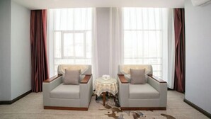 Una habitación con dos sillones, una pequeña mesa redonda y grandes ventanas con cortinas.
