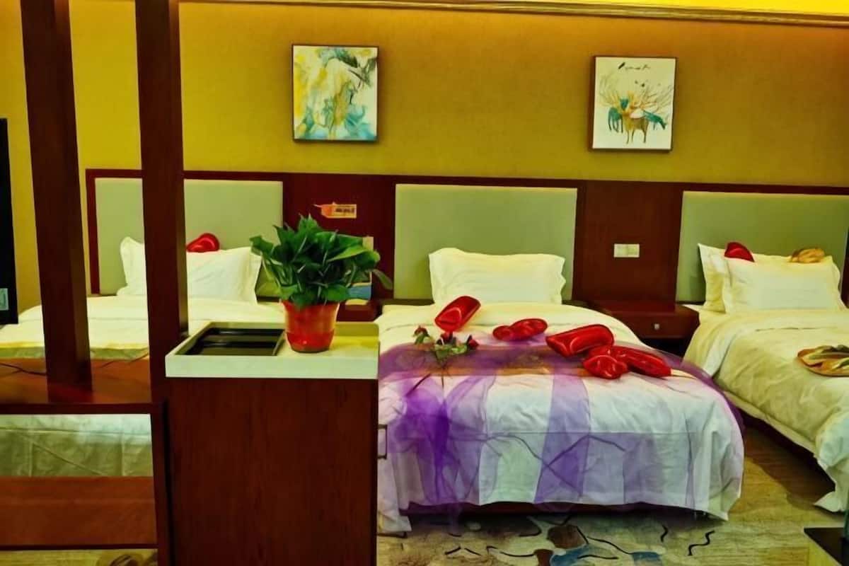 A hotel room with three beds, a potted plant, and artwork on the walls.