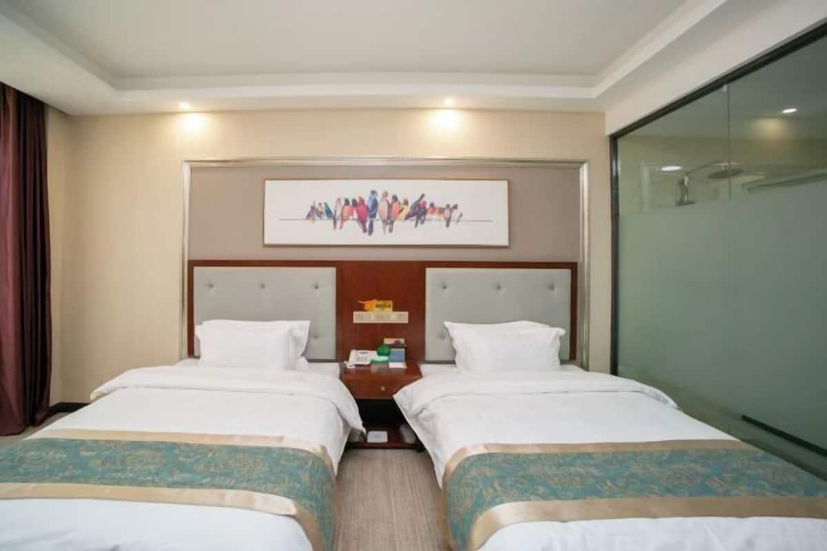 A hotel room with two beds, a headboard with a group portrait, a nightstand, and a glass partition wall.