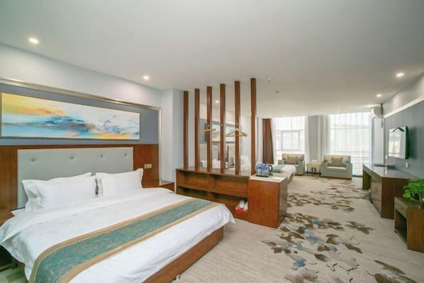 Una habitación de hotel con una cama grande, un cabecero de madera, un escritorio con una silla, un televisor y un ventanal amplio.