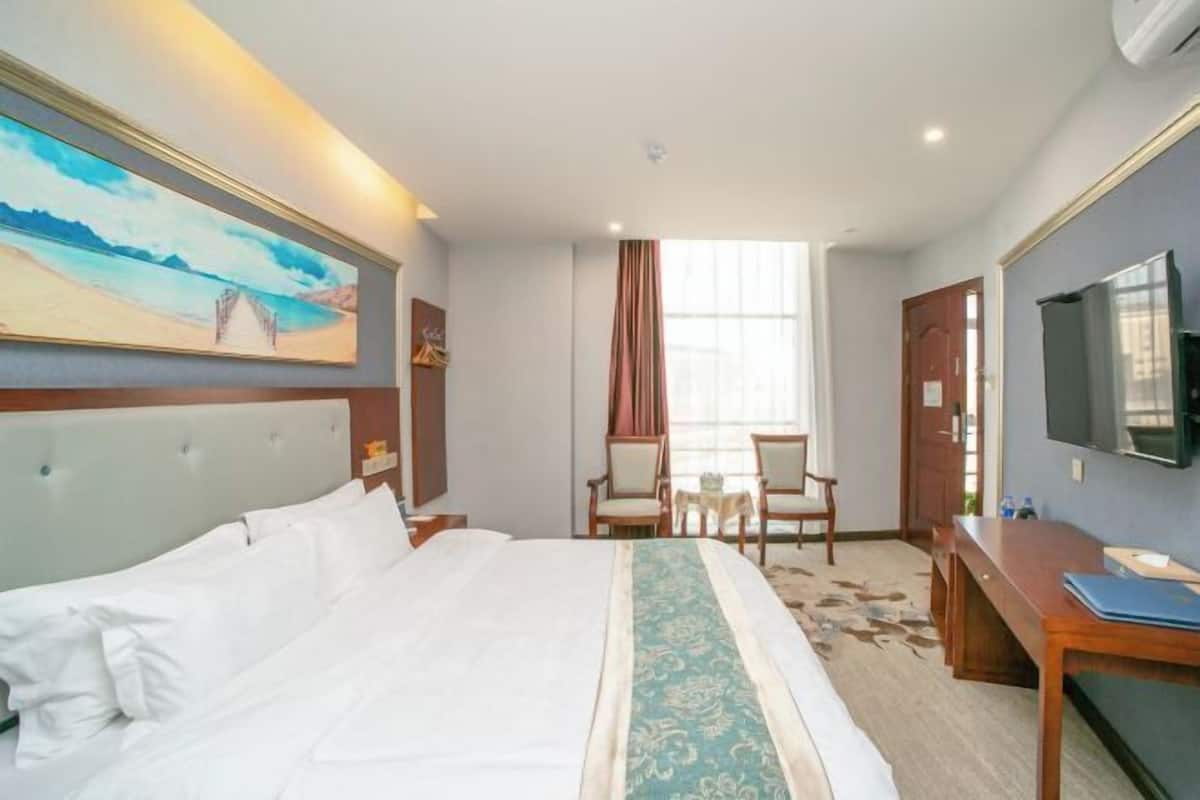 A hotel room with a bed, a desk, a chair, a television, and a painting on the wall.