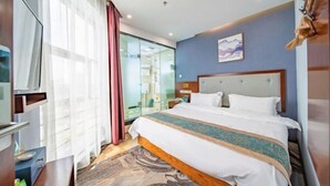 Habitación de hotel con cama, televisión, escritorio y baño visible a través de una puerta de cristal.