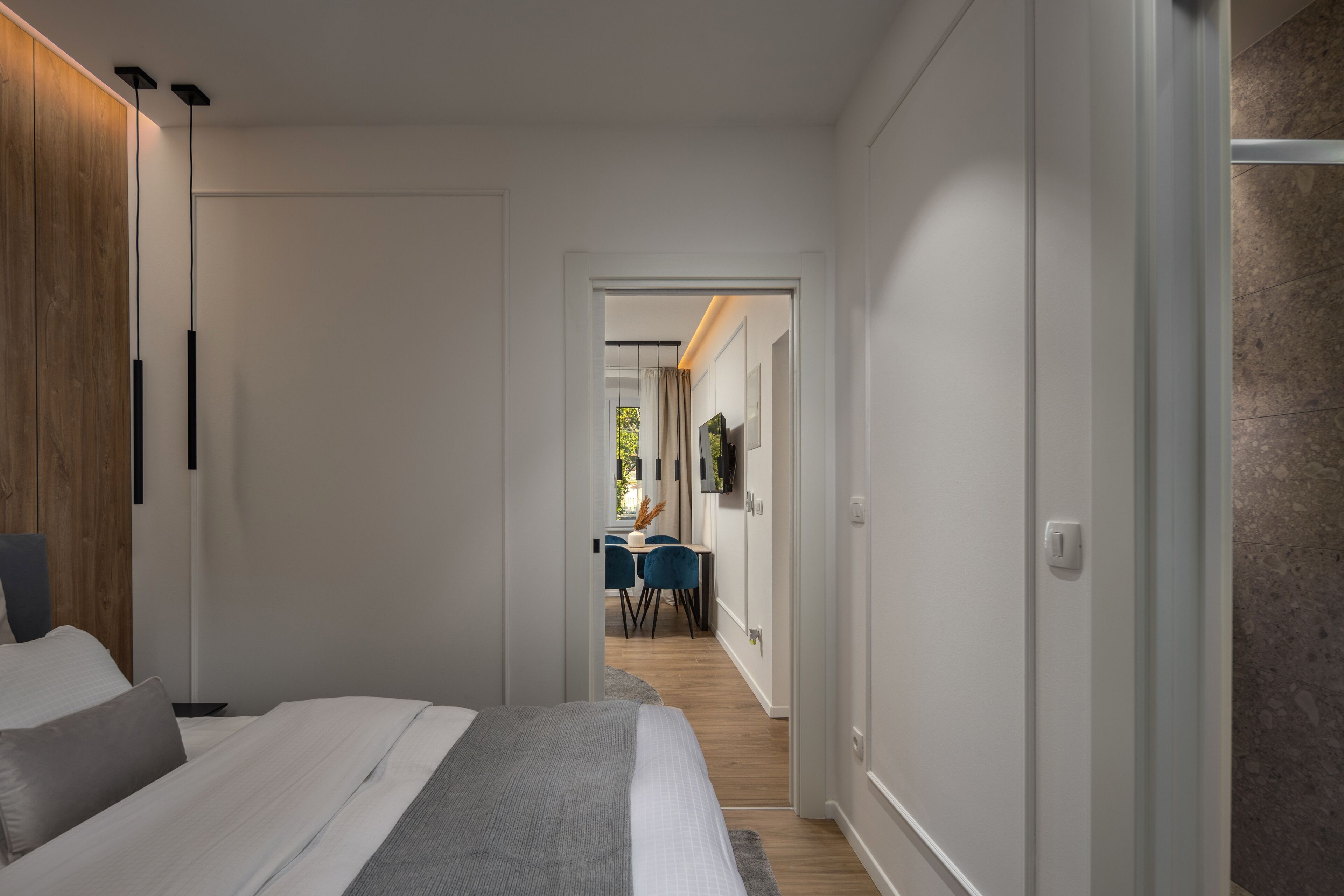 Una habitación de hotel moderna con una cama grande, un armario de madera y un comedor visible a través de una puerta abierta.