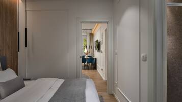 Una habitación de hotel moderna con una cama grande, un armario de madera y un comedor visible a través de una puerta abierta.
