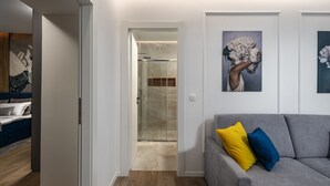 Un salón moderno con un sofá gris, una cabina de ducha de vidrio y obras de arte en las paredes.