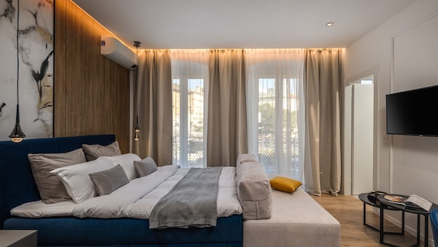 Un dormitorio moderno con una cama grande, un sofá, un televisor y una ventana con cortinas.