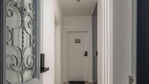Un pasillo con una puerta blanca al final, una reja metálica a la izquierda y piso alfombrado.
