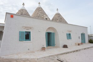 A building with three conical roofs, a white facade, and turquoise shutters. - Trulli in Puglia with Private Forest (Locorotondo BA)