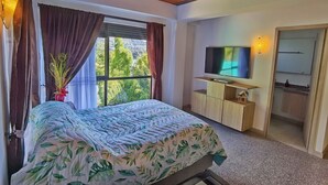 A bedroom with a bed, a TV, a small cabinet, and a window with curtains. - Descanso bajo la Piedra (Guatapé)