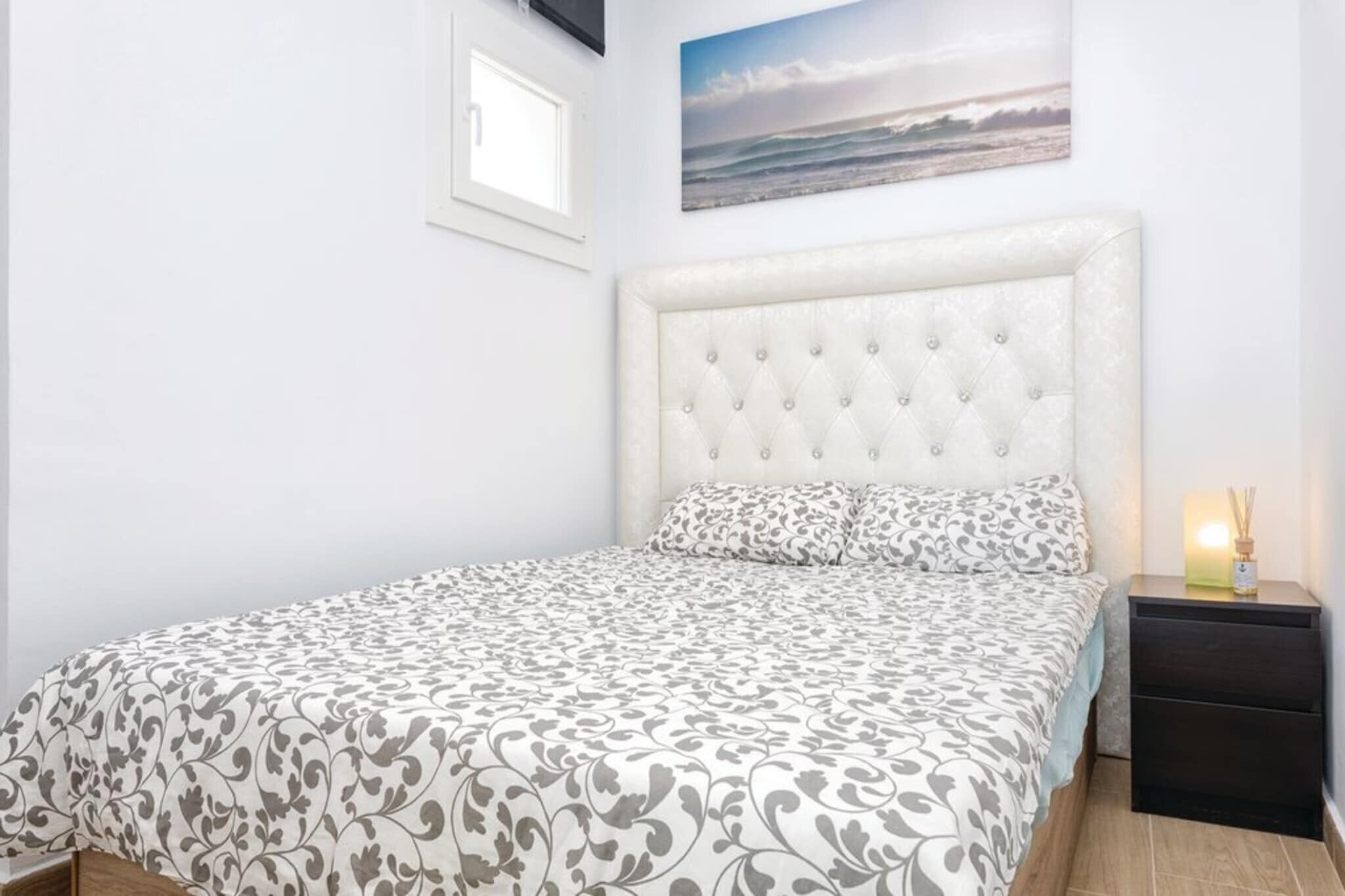 A bedroom with a tufted headboard, patterned bedspread, and a nightstand with a lamp.