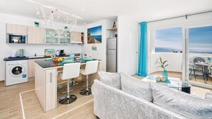 A modern kitchen with a dining area, a sofa, and a balcony with a view.