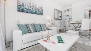 A modern, white-themed living room with a white sofa, a coffee table with decorative items, and a painting on the wall. - Cosy apartment in Mijas (Mijas)