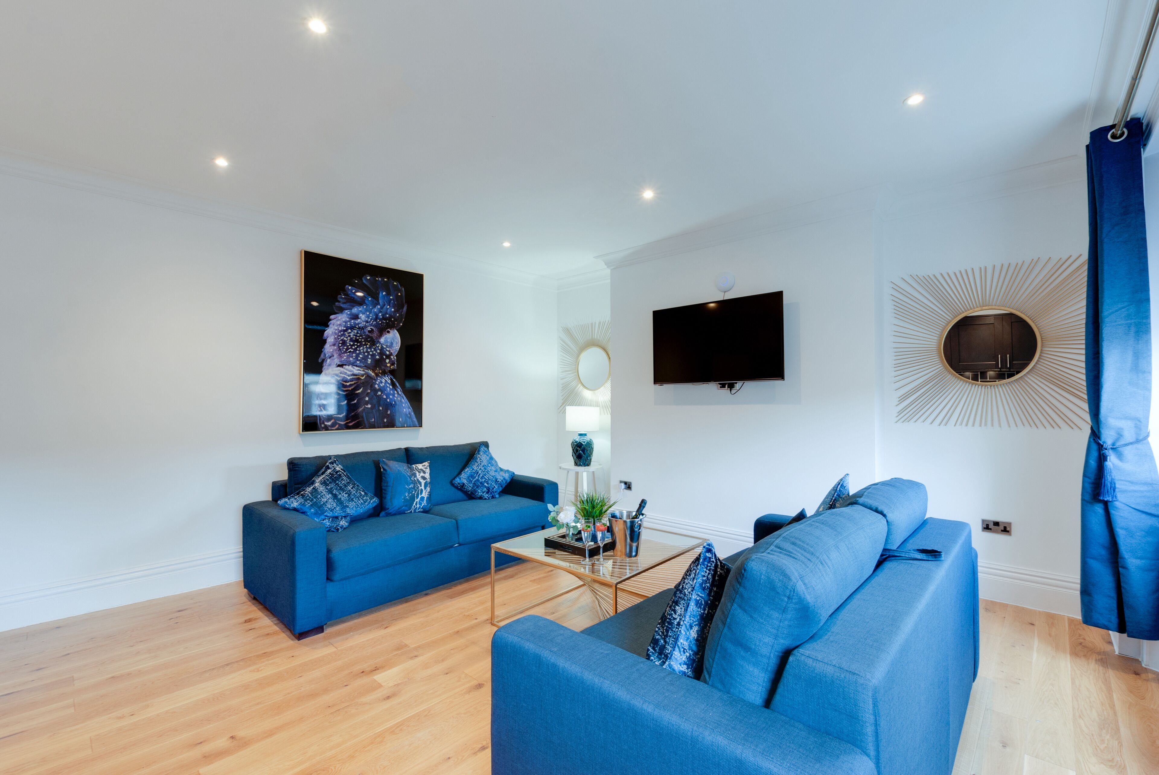 Ein modernes Wohnzimmer mit blauem Sofa, Couchtisch, Flachbildfernseher und einem dekorativen Spiegel.