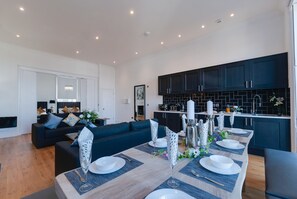 A modern kitchen with dark cabinets and a dining area with a wooden table set for four. - 80 by Elite (Liverpool)