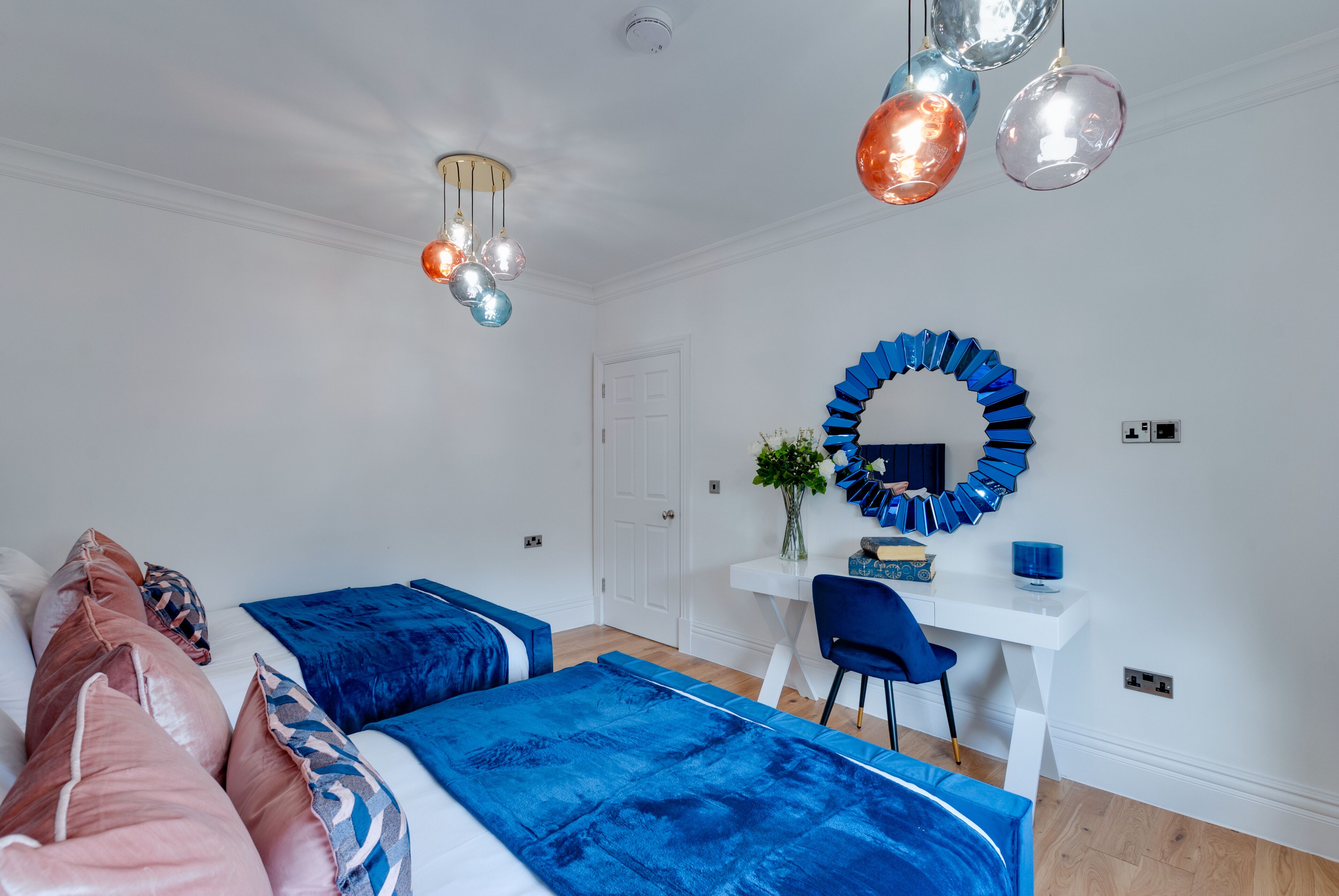 A bedroom with two beds, a desk, a chair, and a mirror.