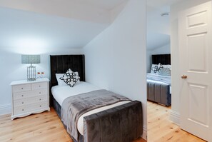 A bedroom with a bed, bedside table, lamp, and a door. - 80 by Elite (Liverpool)