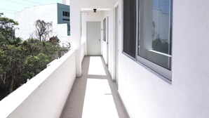 Een smalle, witte gang met grote ramen aan één kant en een balkon aan de andere kant.
