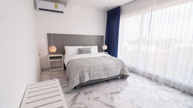 Een moderne hotelkamer met een groot bed, nachtkastje, hanglamp en een groot raam met dunne gordijnen.