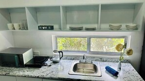 Een keuken met een roestvrijstalen spoelbak, een magnetron en een koffiezetapparaat. Er is een raam boven de spoelbak met uitzicht op groen.
