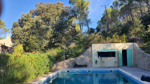 A swimming pool with a stone wall and a small building with a green door. - The Golden Gecko Country House  (Cotignac)