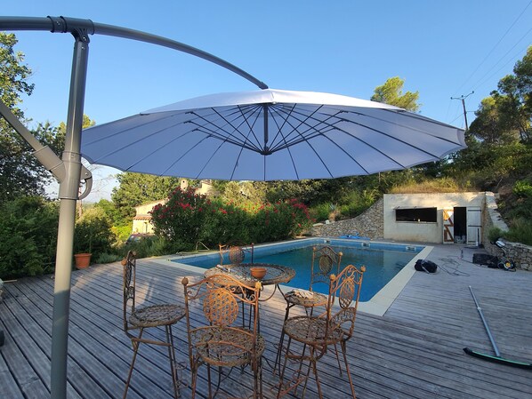 En træterrasse med swimmingpool, havemøbler og en stor parasol.