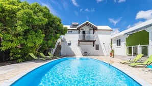 A swimming pool with a clear blue water surface, surrounded by a white building with a balcony and a green wall. - Apartment La Désirade - Sainte-Anne (Sainte-Anne)