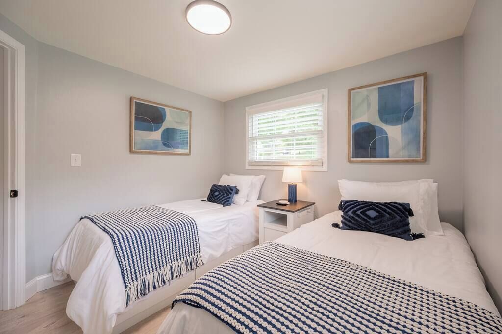 A bedroom with two beds, a nightstand, a lamp, and abstract art on the walls.
