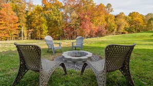 A fire pit surrounded by wicker chairs in a grassy area with autumn-colored trees in the background. - Modern Home 2 Miles to Virginia Tech (Blacksburg)