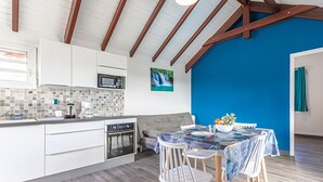 A modern kitchen with white cabinets, a microwave, and a tiled backsplash. There is a dining area with a table set for two, chairs, and a bowl of fruit. - Les Saintes in Sainte-Anne (Sainte-Anne)