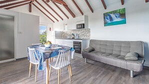 A modern kitchen with a microwave, stove, and tiled backsplash. There is a dining table with chairs and a sofa in the living area. - Les Saintes in Sainte-Anne (Sainte-Anne)