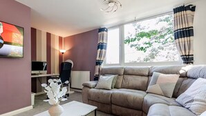 A living room with a sofa, a coffee table, a TV, and a desk with a computer. - Comfortable 3-Storey House with Free Car Parking (Manchester)