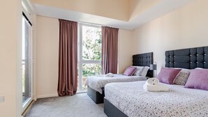 A bedroom with two beds, a large window with curtains, and a view of greenery outside. - Comfortable 3-Storey House with Free Car Parking (Manchester)