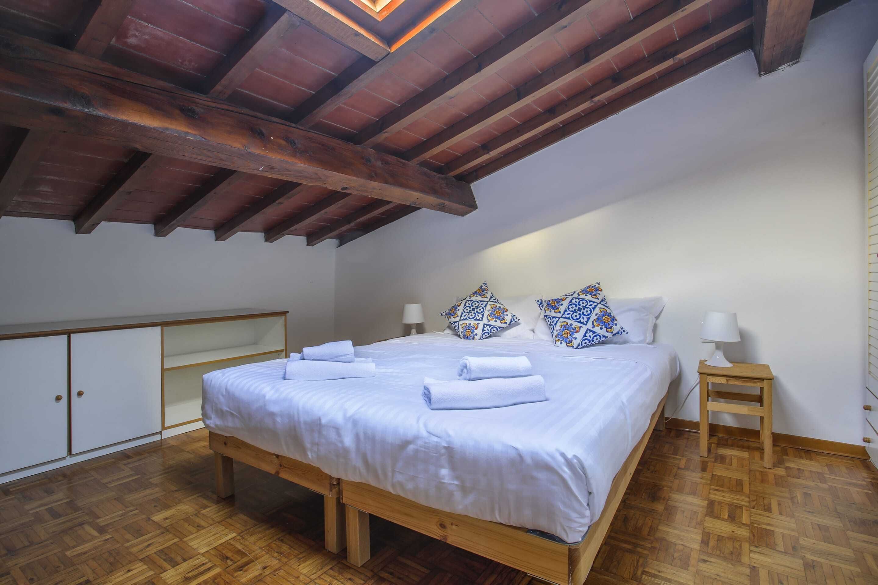 Une chambre à coucher avec un lit en bois, une literie blanche, deux tables de chevet avec des lampes et des coussins à motifs.