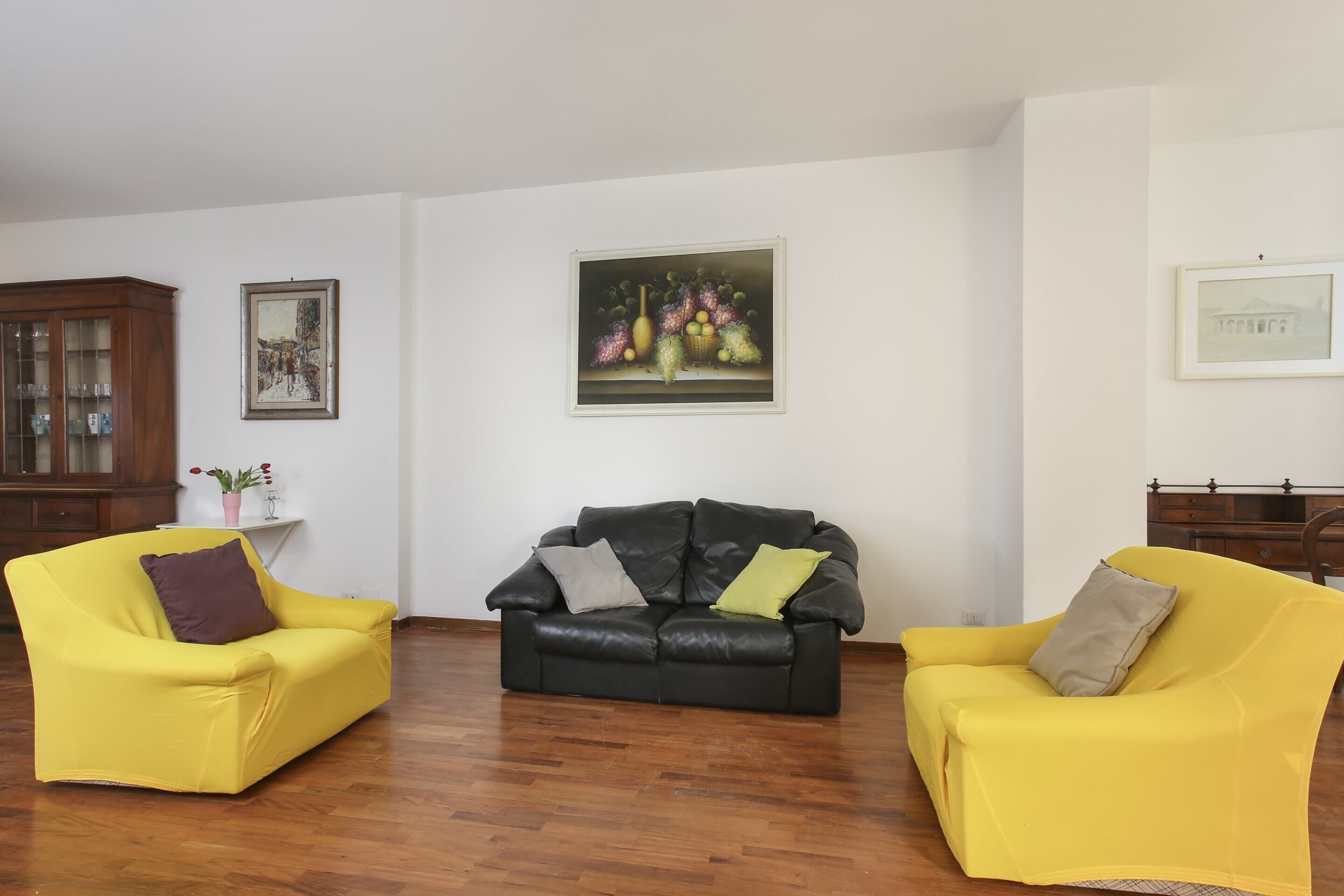 A living room with two yellow armchairs, a black sofa, and a wooden cabinet.