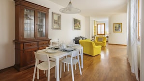 A dining area with a wooden cabinet, white dining table, and chairs. There is a yellow armchair and a gray sofa in the background. - Florence Apartment (Florence)