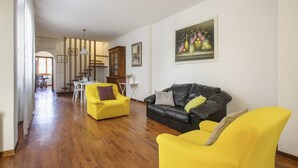 A living room with a wooden floor, yellow armchairs, a black leather sofa, a dining table, and a kitchen in the background. - Florence Apartment (Florence)
