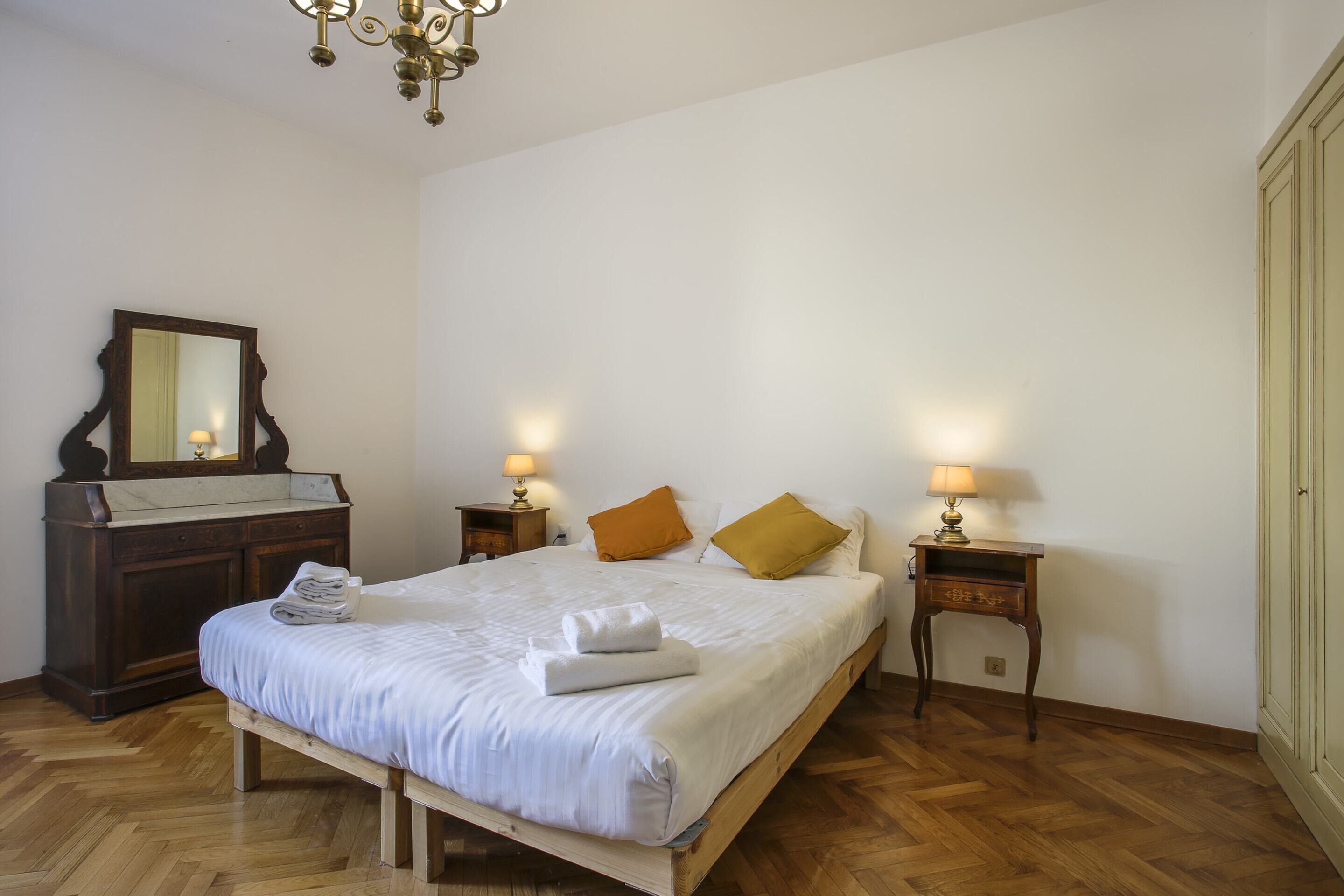 A bedroom with a wooden bed, two nightstands with lamps, a dresser, and a mirror.