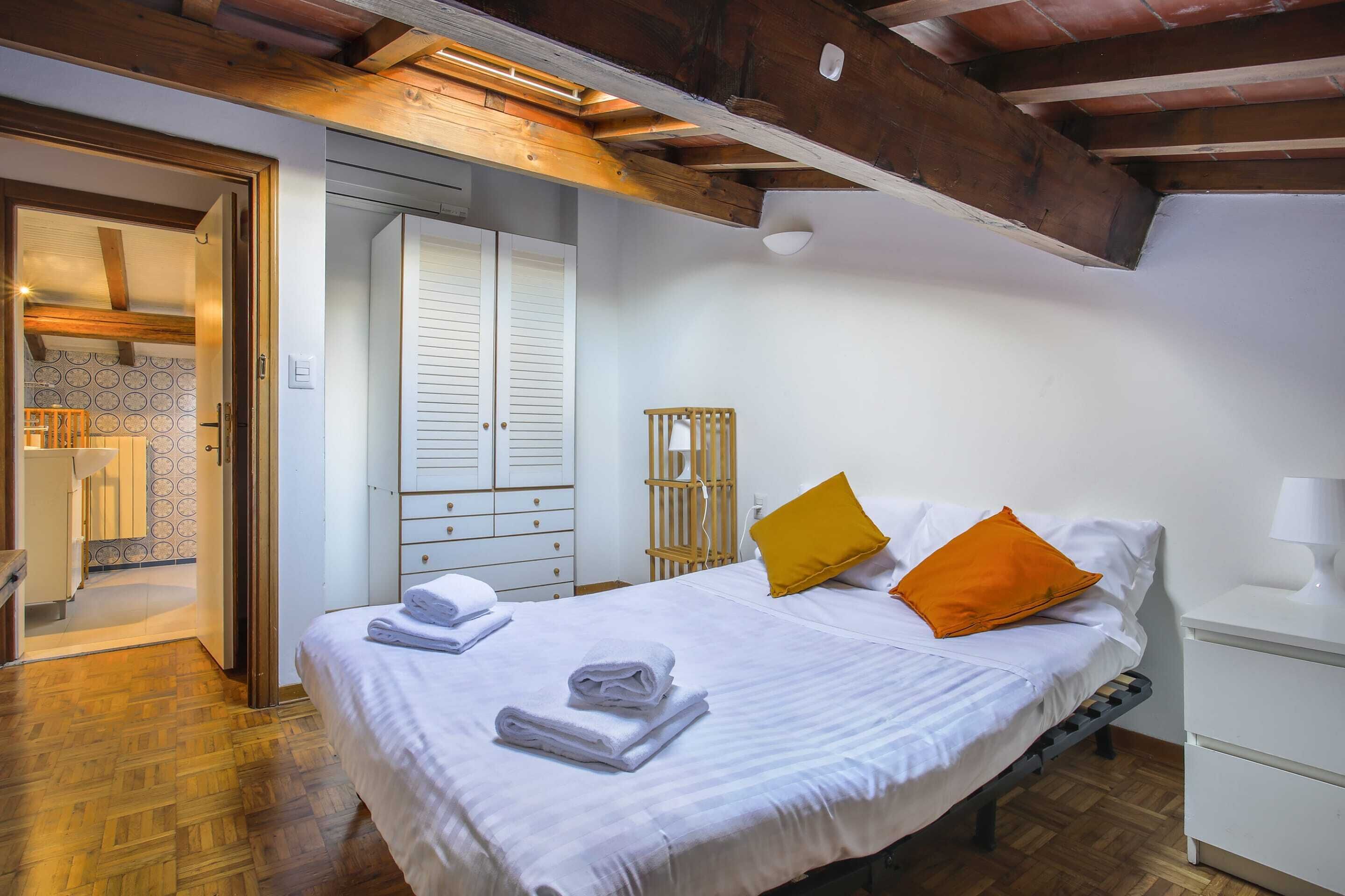 Un dormitorio con una cama, mesitas de noche blancas, un cabecero de madera y un armario.