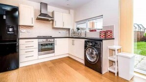A modern kitchen with white cabinetry, a built-in oven, a washing machine, and a small white stool. - VERY CLEAN + AIR CONDITIONING + PARKING + INTERNET (Manchester)