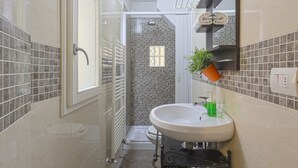 A modern bathroom with a glass-enclosed shower, a white sink with a green soap dispenser, and a potted plant on the countertop.