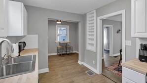 A modern kitchen with a built-in sink, a dining area with a small table and chairs, and a hallway leading to another room.