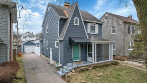 A two-story house with a steeply pitched roof, a front porch with a glass enclosure, and a garage.