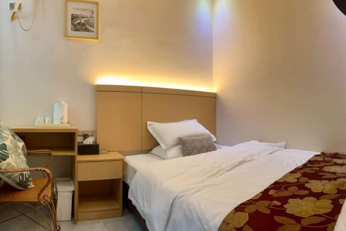 Habitación de hotel ordenada con cama, mesita de noche, silla y estante en la pared.