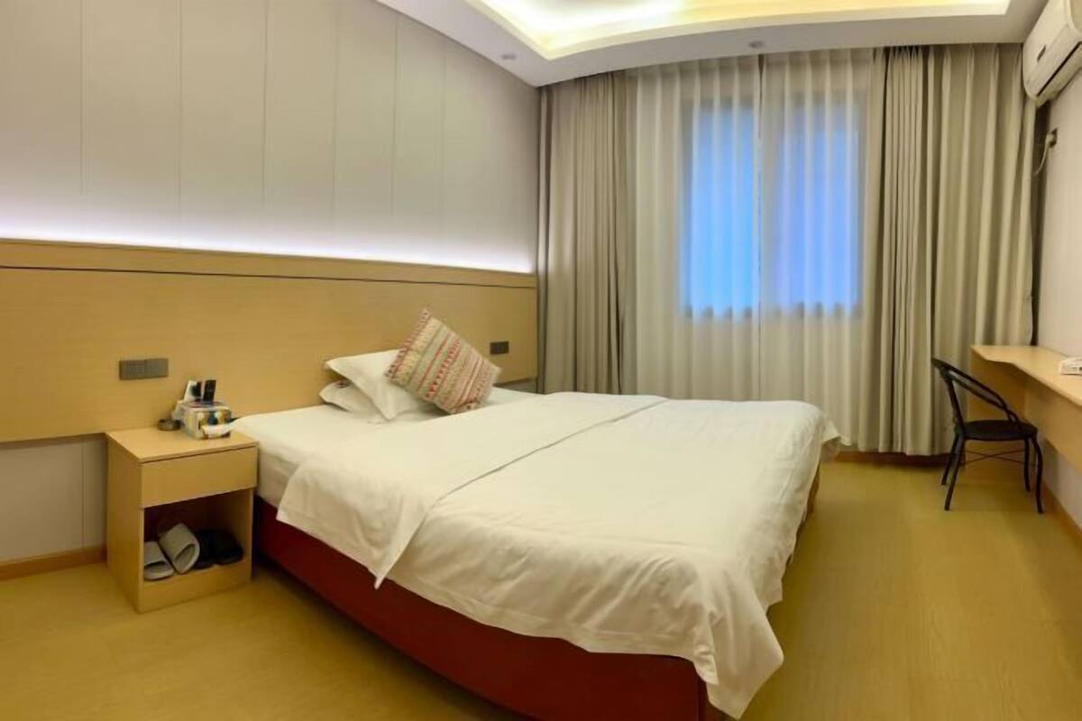 Una habitación de hotel con cama, mesita de noche, escritorio y ventana con cortinas.