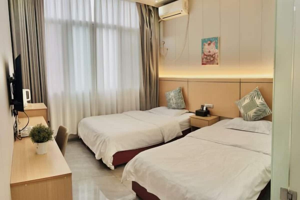 Una habitación de hotel con dos camas, un escritorio con una planta, aire acondicionado y un cuadro en la pared.