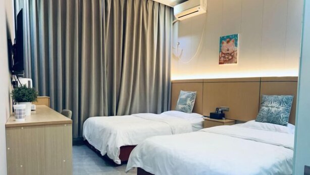 Una habitación de hotel con dos camas, un escritorio, un televisor y aire acondicionado instalado en la pared.