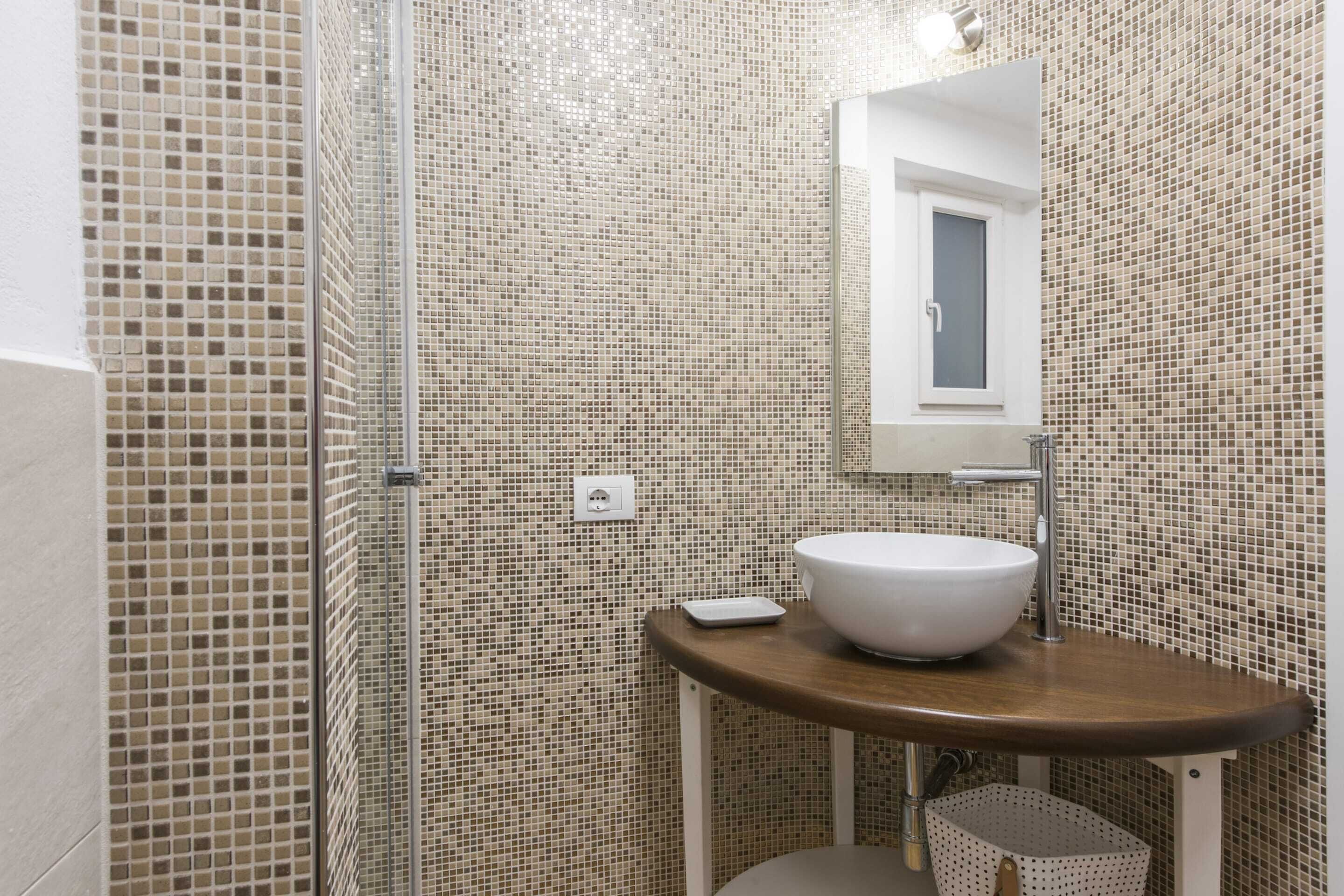 Une salle de bain avec des murs recouverts de mosaïques, un lavabo blanc et un miroir au-dessus.