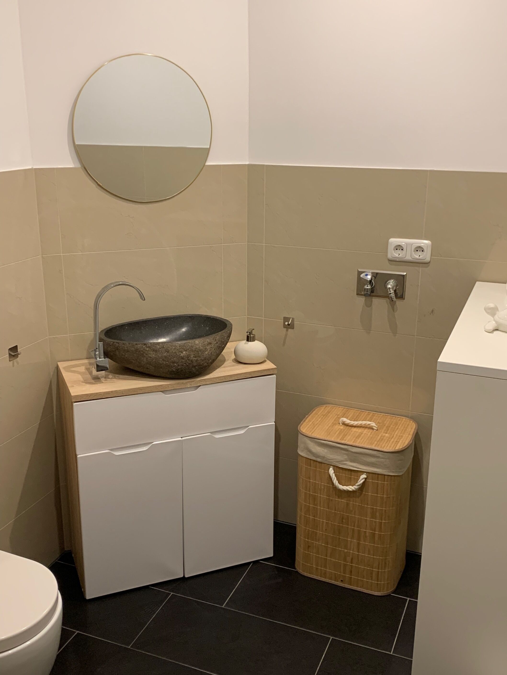 Ein Badezimmer mit rundem Spiegel, einem Aufsatzwaschbecken, einer Toilette und einer kleinen Mülltonne.